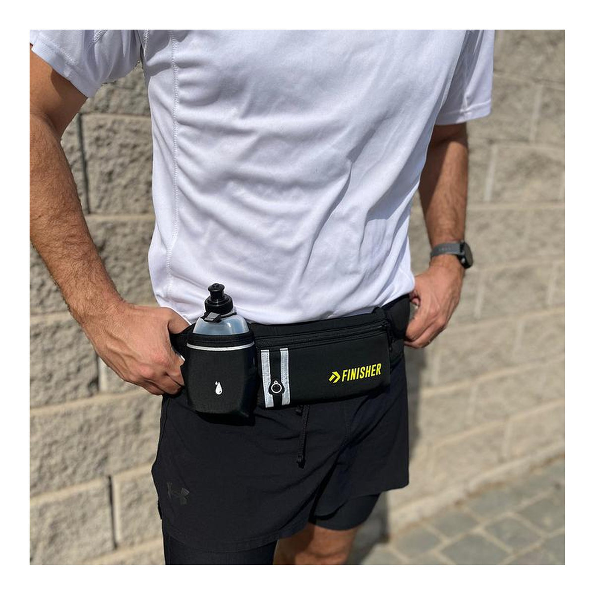 Banano de running Finisher negro puesto en la cintura de un corredor, con la botella de 290 ml a mano