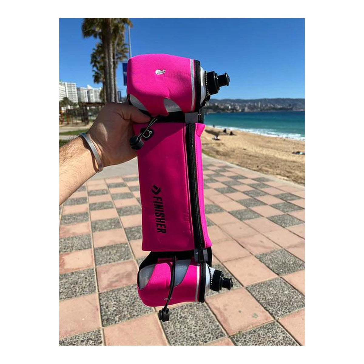 Banano de running Finisher fucsia sostenido en la mano, con sus dos botellas cargadas